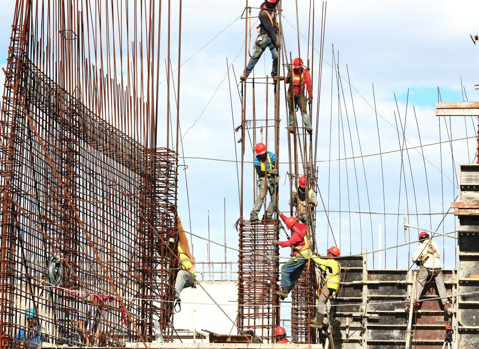 Workers in safety helmets and harnesses fixing rebar columns on site