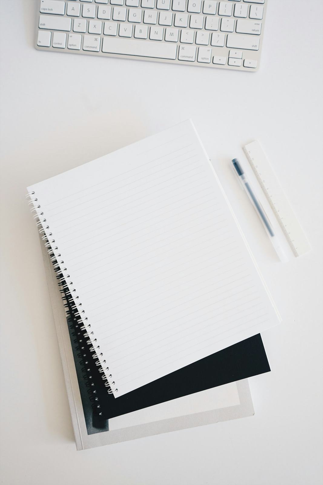 Registers, notebooks, pen and ruler laid out with a keyboard, representing office stationery supplies